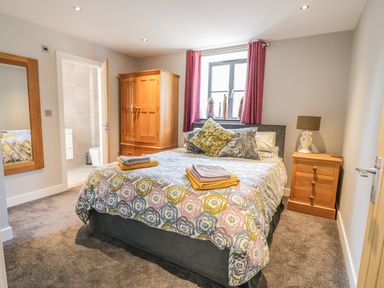A bedroom with a double bed pillows bedside table lamp wooden wardrobe and window at The Coach House in St Columb Major