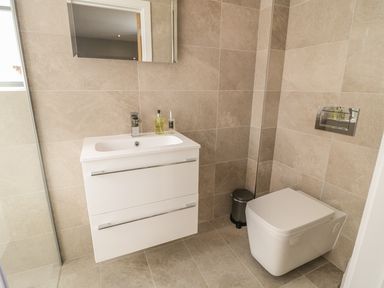 A bathroom with a white sink vanity unit a mirror a toilet and a small trash bin at The Coach House in St Columb Major