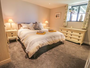A bedroom with a bed with pillows and folded towels bedside tables with lamps a dresser window with curtains and decorative items at The Coach House in St Columb Major