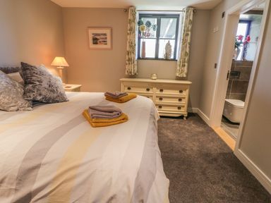 A bedroom with a double bed towels on bed a dresser under a window and an en suite bathroom visible at The Coach House in St Columb Major