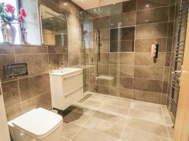 A bathroom with a toilet sink and a walk in shower with brown tiles and a window with flowers at The Coach House in St Columb Major