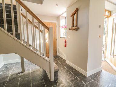 An entryway with tiled floor a staircase with carpet a wooden door a wall mirror and a fire extinguisher at The Coach House in St Columb Major