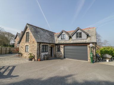 An exterior view of a stone house with a large garage and a paved driveway at The Coach House in St Columb Major