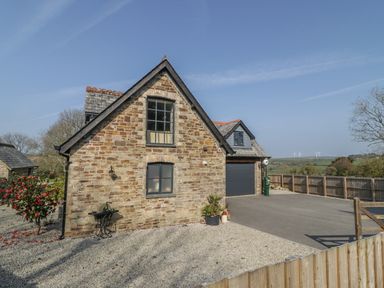 A stone house with two windows and a garage surrounded by gravel and a wooden fence at The Coach House in St Columb Major