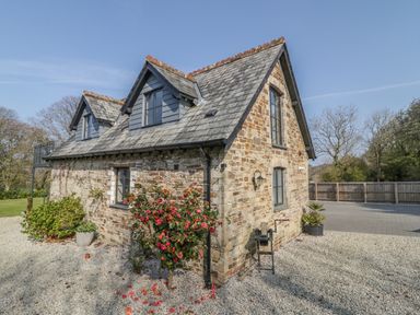 A stone house with a tiled roof and two dormer windows with plants and gravel around at The Coach House in St Columb Major