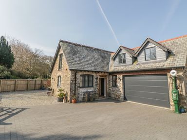 A stone house with a slate roof a large garage door and a vintage green petrol pump outside