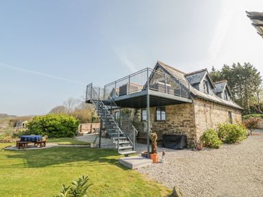 A stone house with an external metal staircase leading to a balcony and a garden with a picnic table at The Coach House in St Columb Major