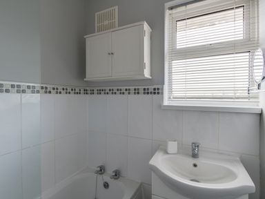 A bathroom with a bathtub a sink a wall cabinet and a window with blinds at The Lookout -The House With A View in Weymouth