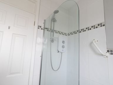 A shower area with a glass screen white tiles and a grab bar at The Lookout -The House With A View in Weymouth