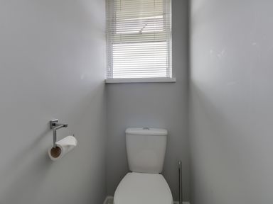 A toilet with a toilet paper holder and a window with blinds at The Lookout -The House With A View in Weymouth