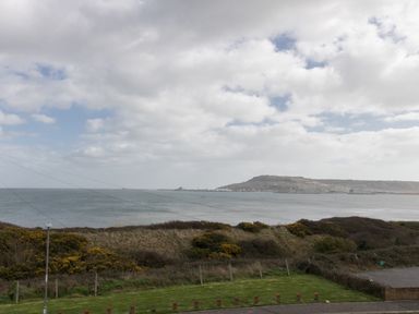 A coastal view with grassy bushes and a hill across the water at The Lookout -The House With A View in Weymouth