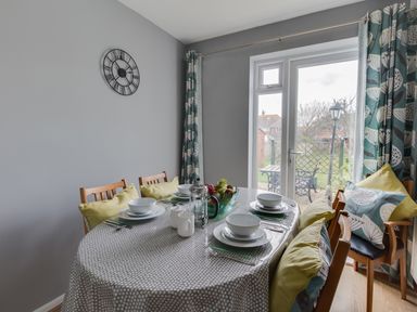 A dining room with a round table set for four and glass doors leading to a garden at The Lookout -The House With A View in Weymouth