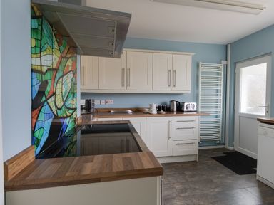 A kitchen with wooden countertops white cabinets a colorful backsplash and kitchen appliances at The Lookout -The House With A View in Weymouth
