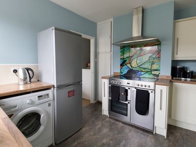 A kitchen with a washing machine a refrigerator a stainless steel stove with oven and a colorful tiled backsplash at The Lookout -The House With A View in Weymouth