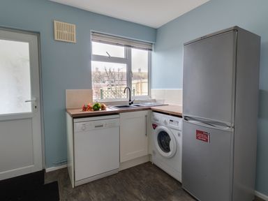 A kitchen corner with a dishwasher washing machine refrigerator sink and door at The Lookout -The House With A View in Weymouth