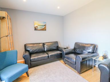 A living room with black leather sofas a blue chair a carpet a wooden cabinet and a landscape painting at The Lookout -The House With A View in Weymouth