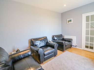 A living room with three black leather armchairs wooden floor a carpet a radiator and a door with glass panels at The Lookout -The House With A View in Weymouth
