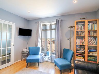 A sitting room with two blue chairs a glass cabinet with books and games and a wall-mounted tv at The Lookout -The House With A View in Weymouth