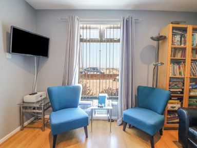 A room with two blue chairs a glass side table a wall mounted TV and a bookcase at The Lookout -The House With A View in Weymouth