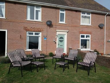 A garden with chairs in front of a brick house at The Lookout -The House With A View Weymouth
