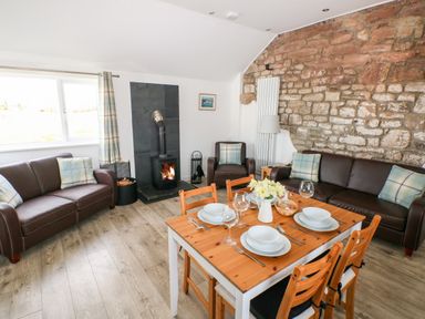 A living room with two brown leather sofas a wooden dining table set with plates and glasses a stone wall and a wood burning stove at Dairy Cottage Tavernspite near Narberth