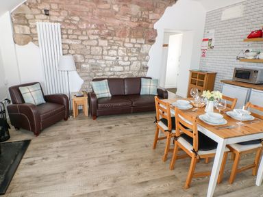 A living room with brown leather sofa and armchair next to a wooden dining table with chairs and tableware at Dairy Cottage in Tavernspite near Narberth