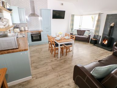 An open plan kitchen and living area with a dining table set a wood burner and sofas at Dairy Cottage Tavernspite near Narberth