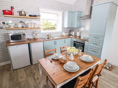 A kitchen with light blue cabinets a wooden dining table set for four and kitchen appliances at Dairy Cottage Tavernspite near Narberth