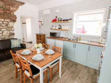A kitchen dining area with a wooden table set for four beside a sofa and a counter with blue cabinets at Dairy Cottage Tavernspite near Narberth
