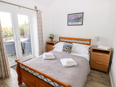 A bedroom with a double bed two wooden bedside tables with lamps folded towels and glass doors leading outside at Dairy Cottage Tavernspite near Narberth