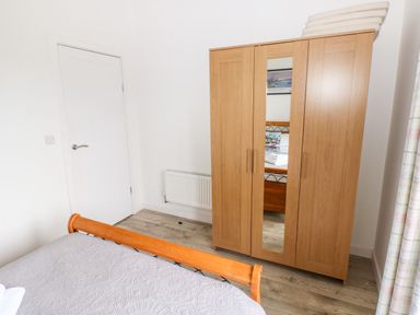 A bedroom with a wooden bed, a three door wooden wardrobe with a mirror, folded towels on top, a white door and a radiator at Dairy Cottage Tavernspite near Narberth