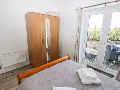 A bedroom with a wooden wardrobe with a mirror a bed with folded white towels and glass doors leading outside at Dairy Cottage in Tavernspite near Narberth
