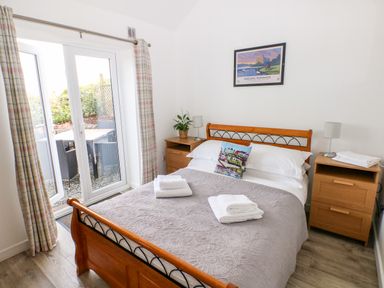 A bedroom with a double bed, two bedside tables with lamps, folded towels on the bed, a plant, and glass doors leading outside at Dairy Cottage Tavernspite near Narberth