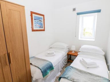 A small bedroom with two single beds a wooden wardrobe and a window at Dairy Cottage in Tavernspite near Narberth