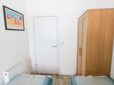 A bedroom with a white door wooden wardrobe radiator and two beds with blue and gray blankets at Dairy Cottage Tavernspite near Narberth
