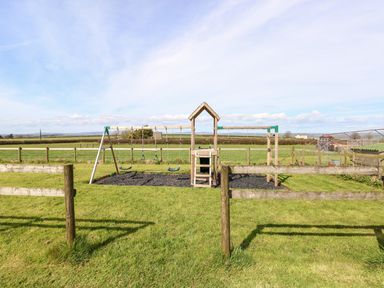 A children's wooden swing set and climbing frame in a fenced grassy field at Dairy Cottage Tavernspite near Narberth