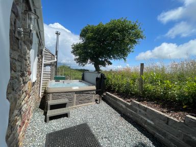 An outdoor area with a hot tub next to a stone wall and a garden with plants and a tree at Dairy Cottage in Tavernspite near Narberth