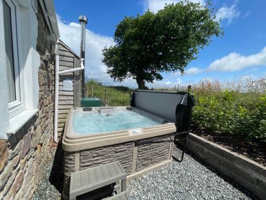An outdoor hot tub next to a stone wall with gravel ground and greenery at Dairy Cottage Tavernspite near Narberth