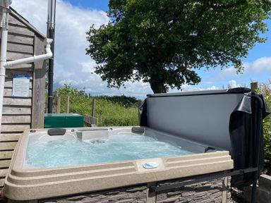 An outdoor hot tub with bubbling water next to a wooden building and a large tree at Dairy Cottage Tavernspite near Narberth