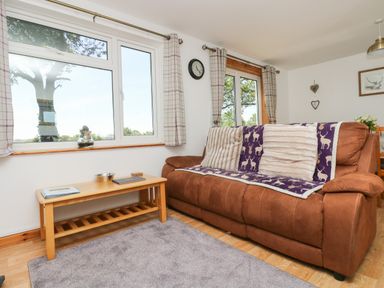 A living room with a brown sofa and a wooden coffee table by windows at Dartmoor 2 in Callington