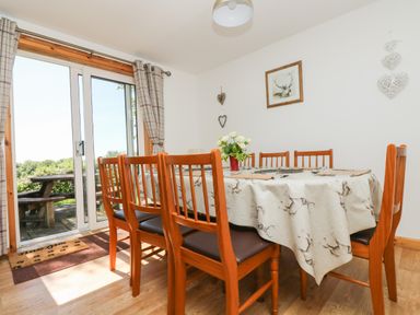 A dining room with a wooden table covered with a patterned tablecloth and six wooden chairs near glass sliding doors at Dartmoor 2 Callington