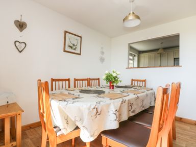 A dining room with a wooden table and chairs with a deer patterned tablecloth at Dartmoor 2 in Callington