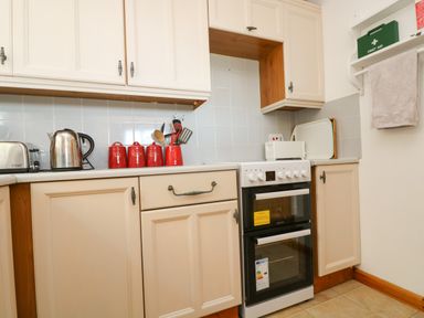 A kitchen with cream cabinets a kettle a toaster red canisters a stove and a microwave at Dartmoor 2 in Callington