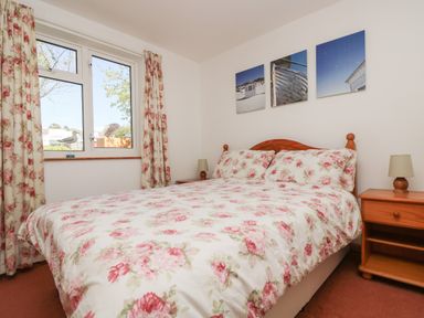 A bedroom with a floral bedspread on a double bed beside a window with floral curtains and wooden nightstands at Dartmoor 2 in Callington