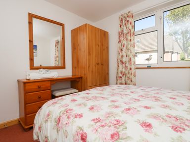 A bedroom with a wooden dresser mirror wardrobe and floral curtains at Dartmoor 2 in Callington