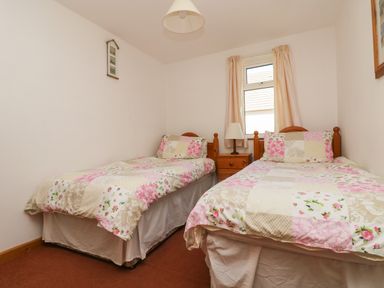 A bedroom with two single beds with floral bedspreads and a wooden nightstand with a lamp between them at Dartmoor 2 in Callington