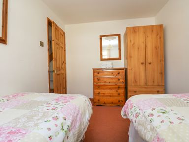 A bedroom with two beds, a wooden dresser, a wardrobe, a mirror, and an open door at Dartmoor 2 in Callington