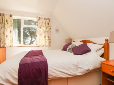 A bedroom with a bed with white and purple bedding two bedside tables with lamps and floral curtains at Dartmoor 2 in Callington