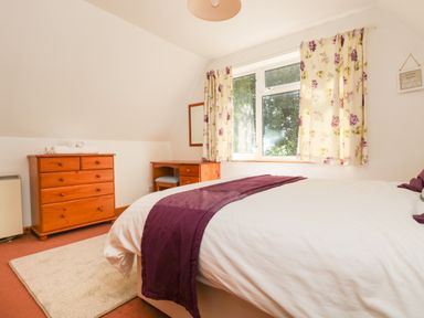 A bedroom with a bed near a window with floral curtains and wooden furniture at Dartmoor 2 in Callington