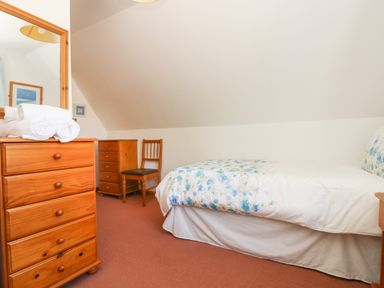 A bedroom with a single bed with blue floral bedding a wooden chair two wooden dressers and a mirror at Dartmoor 2 in Callington
